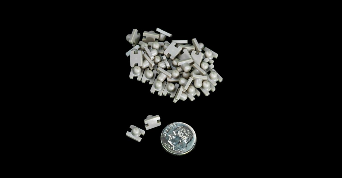 Small white plastic machined components displayed on a black background, with a dime included for size comparison.