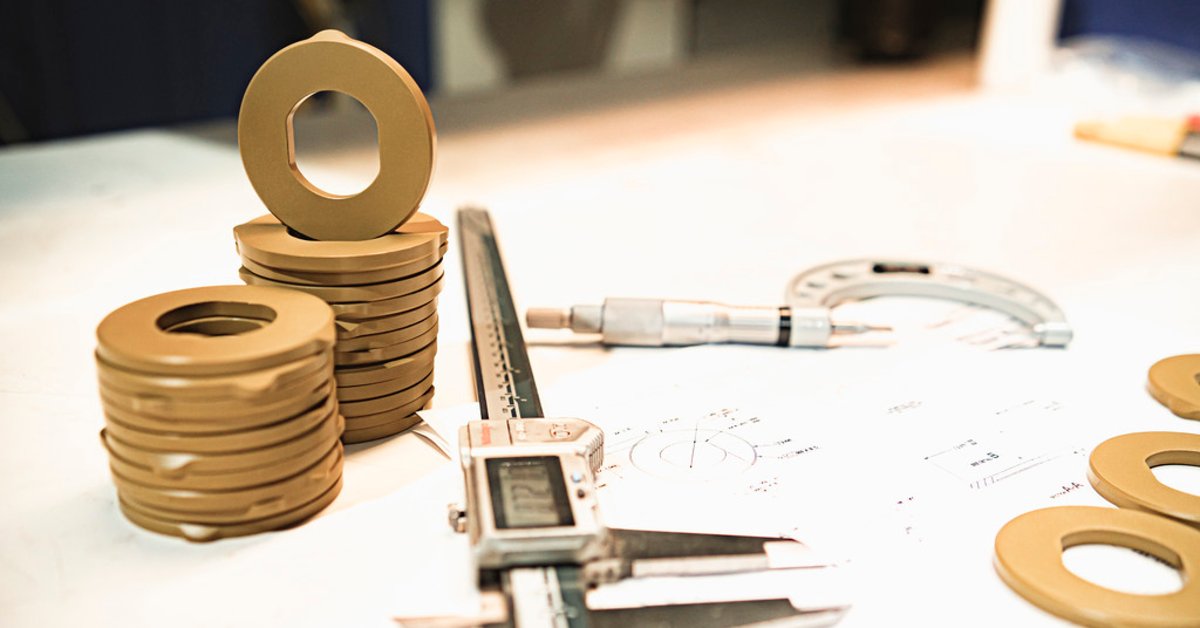 Precision-machined plastic components with measuring tools, calipers, and engineering drawings on a workbench.