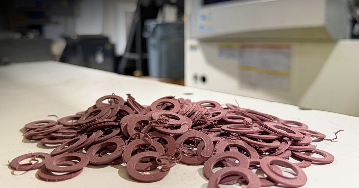 Brown Rulon® rings sit on a white table in an industrial environment. Small strips of material sit among the rings. | Plastic Machining Inc. Brown Rulon® rings sit on a white table in an industrial environment. Small strips of material sit among the rings.