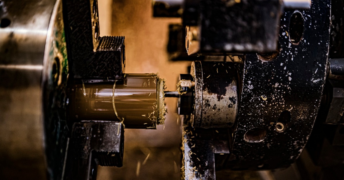 A metal lathe cutting a cylindrical part with shavings scattered around the tool and surrounding machine components. | Plastic Machining Inc. A metal lathe cutting a cylindrical part with shavings scattered around the tool and surrounding machine components.