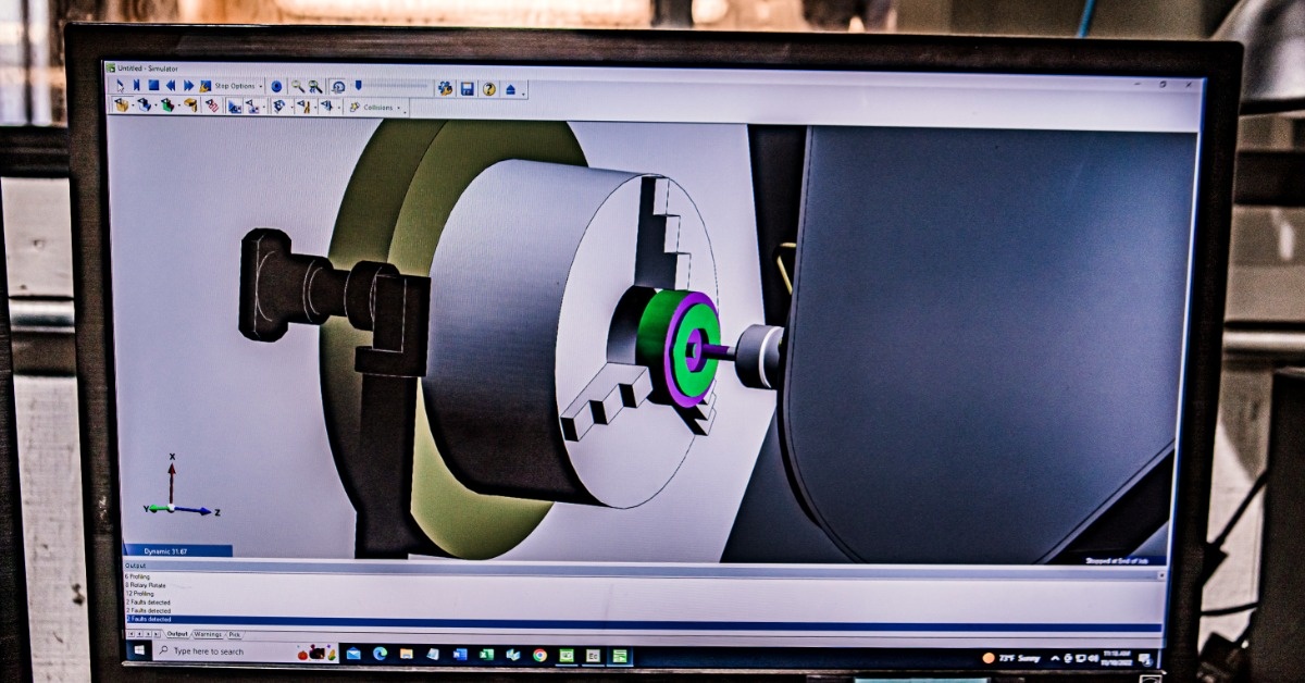 A monitor showing a 3D machining simulation with a lathe chuck, cutting tool, colored part, and software menus.