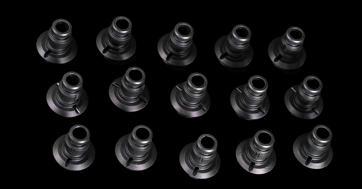 Rows of black machined plastic parts arranged on a dark surface with hollow centers and circular bases.
