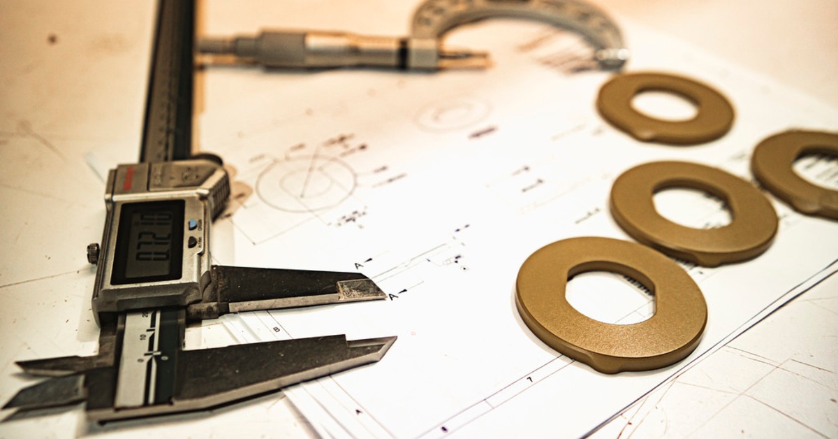 7 Best Plastics for Continuous High Heat Exposure | Plastic Machining Inc. Digital calipers and tan ring-shaped parts resting on a technical drawing with measurement markings and notes.